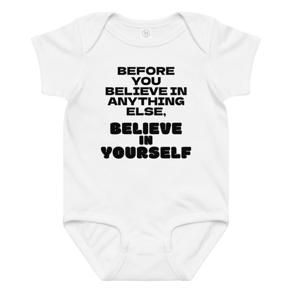 "Before you believe in anything else, believe in yourself" printed on a white baby jersey bodysuit laying on a flat surface amongst other clothes