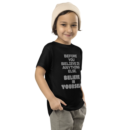 "Before you believe in anything else, believe in yourself" printed on a black toddler short sleeve tee worn by a male who is also wearing a knit cap