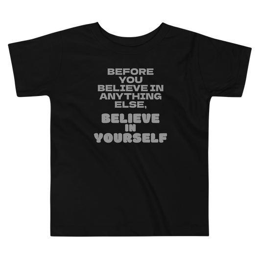 "Before you believe in anything else, believe in yourself" printed on a black toddler short sleeve tee laying on a flat surface