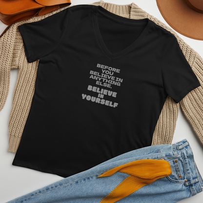 "Before you believe in anything else, believe in yourself" printed on a solid black blend women's relaxed v-neck t-shirt laying on a flat surface amongst other clothes
