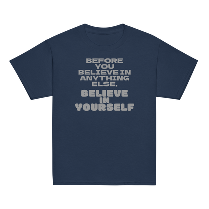 "Before you believe in anything else, believe in yourself" printed on a navy youth classic tee laying on a flat surface