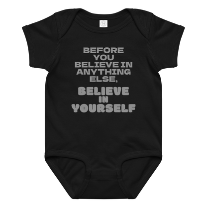 "Before you believe in anything else, believe in yourself" printed on a black baby jersey bodysuit laying on a flat surface amongst other clothes