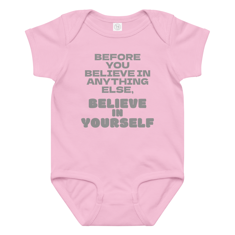"Before you believe in anything else, believe in yourself" printed on a pink baby jersey bodysuit laying on a flat surface amongst other clothes