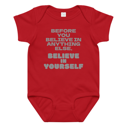 "Before you believe in anything else, believe in yourself" printed on a red baby jersey bodysuit laying on a flat surface amongst other clothes