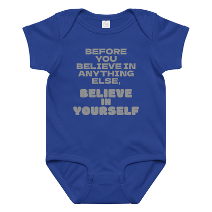 "Before you believe in anything else, believe in yourself" printed on a royal baby jersey bodysuit laying on a flat surface amongst other clothes
