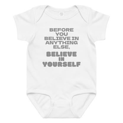 "Before you believe in anything else, believe in yourself" printed on a white baby jersey bodysuit laying on a flat surface amongst other clothes