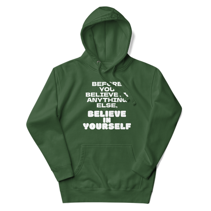 "Before you believe in anything else, believe in yourself" printed on a forest green unisex hoodie laying on a flat surface with the hood up
