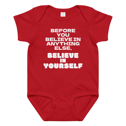 "Before you believe in anything else, believe in yourself" printed on a red baby jersey bodysuit laying on a flat surface amongst other clothes