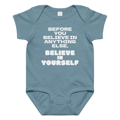 "Before you believe in anything else, believe in yourself" printed on a vintage indigo baby jersey bodysuit laying on a flat surface amongst other clothes