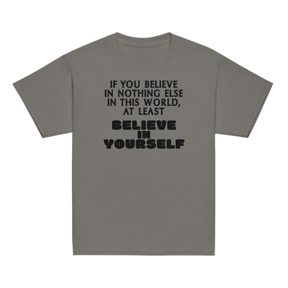 "If you believe in nothing else in this world, at least believe in yourself" printed on a charcoal youth classic tee laying on a flat surface