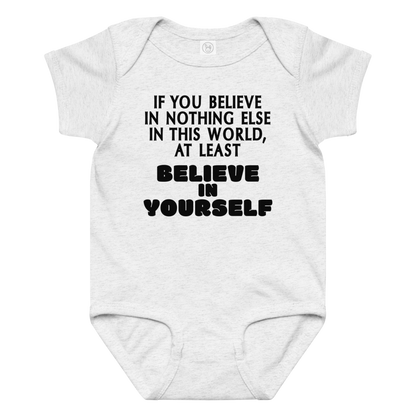 "If you believe in nothing else in this world, at least believe in yourself" printed on a ash baby jersey bodysuit laying on a flat surface amongst other clothes