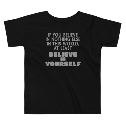 "If you believe in nothing else in this world, at least believe in yourself" printed on a black toddler short sleeve tee laying on a flat surface