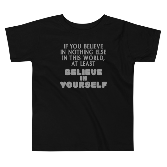 "If you believe in nothing else in this world, at least believe in yourself" printed on a black toddler short sleeve tee laying on a flat surface