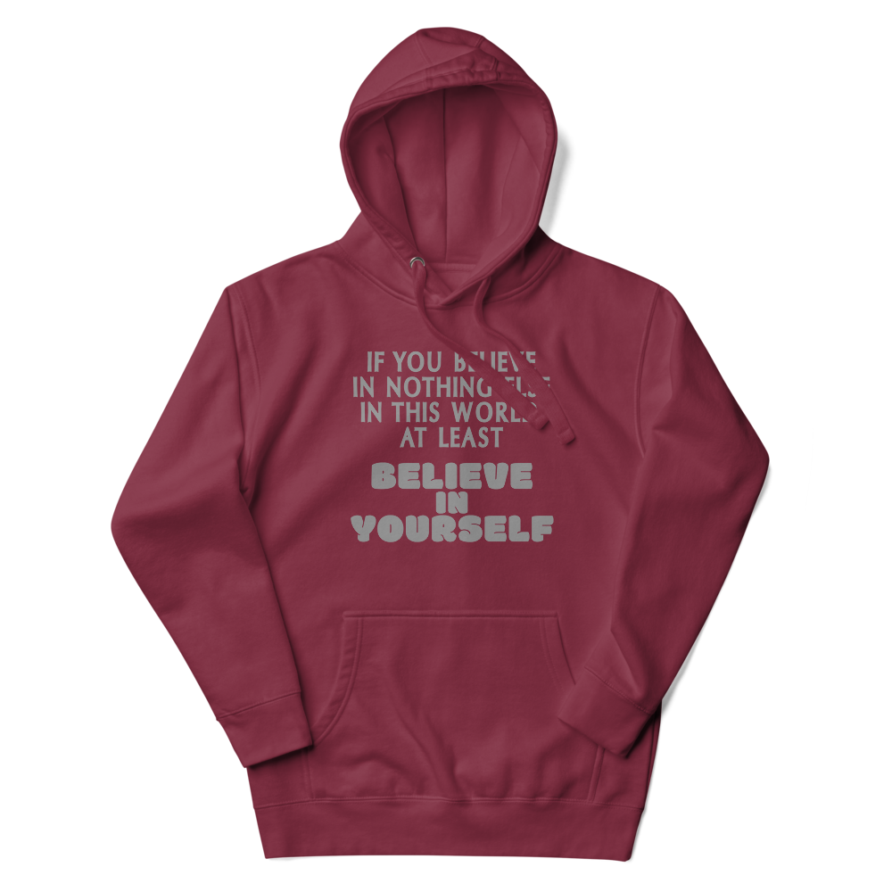 "If you believe in nothing else in this world, at least believe in yourself" printed on a maroon unisex hoodie laying on a flat surface with the hood up