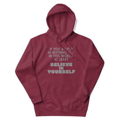 "If you believe in nothing else in this world, at least believe in yourself" printed on a maroon unisex hoodie laying on a flat surface with the hood up