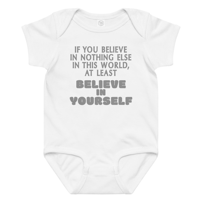 "If you believe in nothing else in this world, at least believe in yourself" printed on a white baby jersey bodysuit laying on a flat surface amongst other clothes