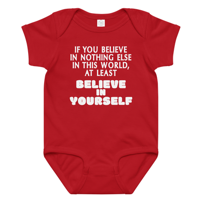 "If you believe in nothing else in this world, at least believe in yourself" printed on a red baby jersey bodysuit laying on a flat surface amongst other clothes