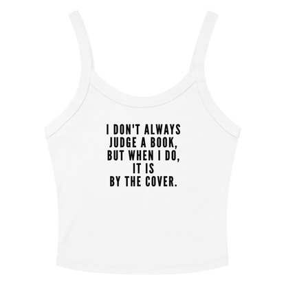 "I Don't always Judge a Book, but when I do, it's by the cover." printed on a solid white blend women's micro-rib tanktop laying on a flat surface amongst sunglasses and shorts