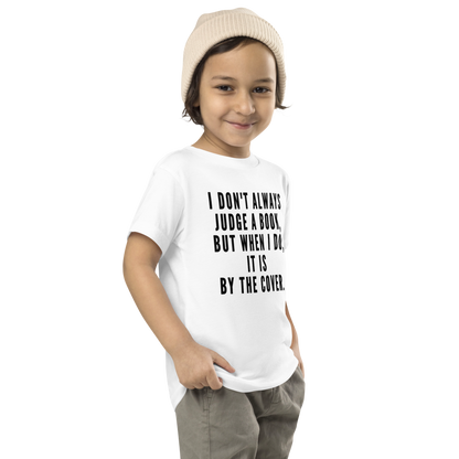 "I Don't always Judge a Book, but when I do, it's by the cover." printed on a white toddler short sleeve tee worn by a male who is also wearing a knit cap