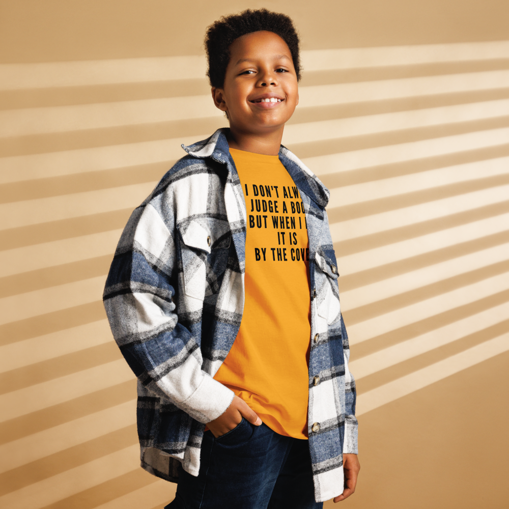 "I Don't always Judge a Book, but when I do, it's by the cover." printed on a gold youth classic tee worn by a male also wearing a jacket