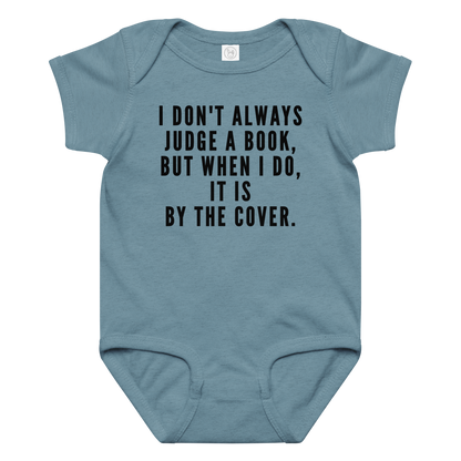 "I Don't always Judge a Book, but when I do, it's by the cover." printed on a vintage indigo baby jersey bodysuit laying on a flat surface amongst other clothes