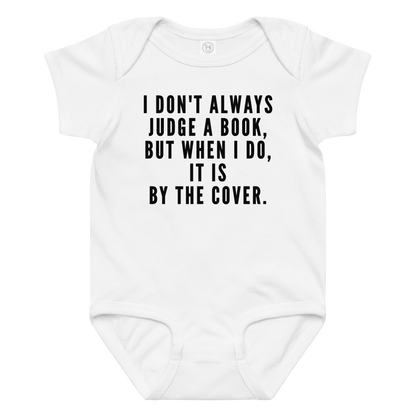 "I Don't always Judge a Book, but when I do, it's by the cover." printed on a white baby jersey bodysuit laying on a flat surface amongst other clothes