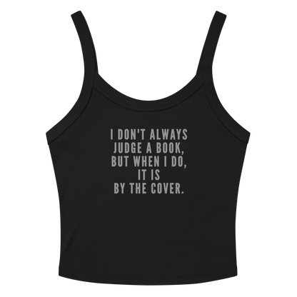 "I Don't always Judge a Book, but when I do, it's by the cover." printed on a solid black blend women's micro-rib tanktop laying on a flat surface amongst sunglasses and shorts