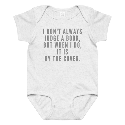 "I Don't always Judge a Book, but when I do, it's by the cover." printed on a ash baby jersey bodysuit laying on a flat surface amongst other clothes