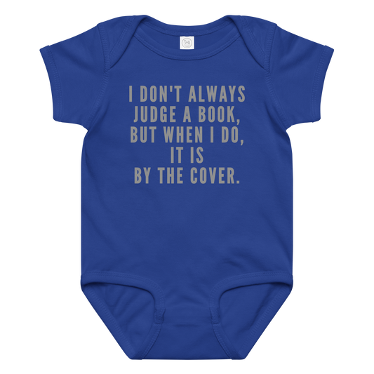 "I Don't always Judge a Book, but when I do, it's by the cover." printed on a royal baby jersey bodysuit laying on a flat surface amongst other clothes
