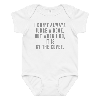 "I Don't always Judge a Book, but when I do, it's by the cover." printed on a white baby jersey bodysuit laying on a flat surface amongst other clothes