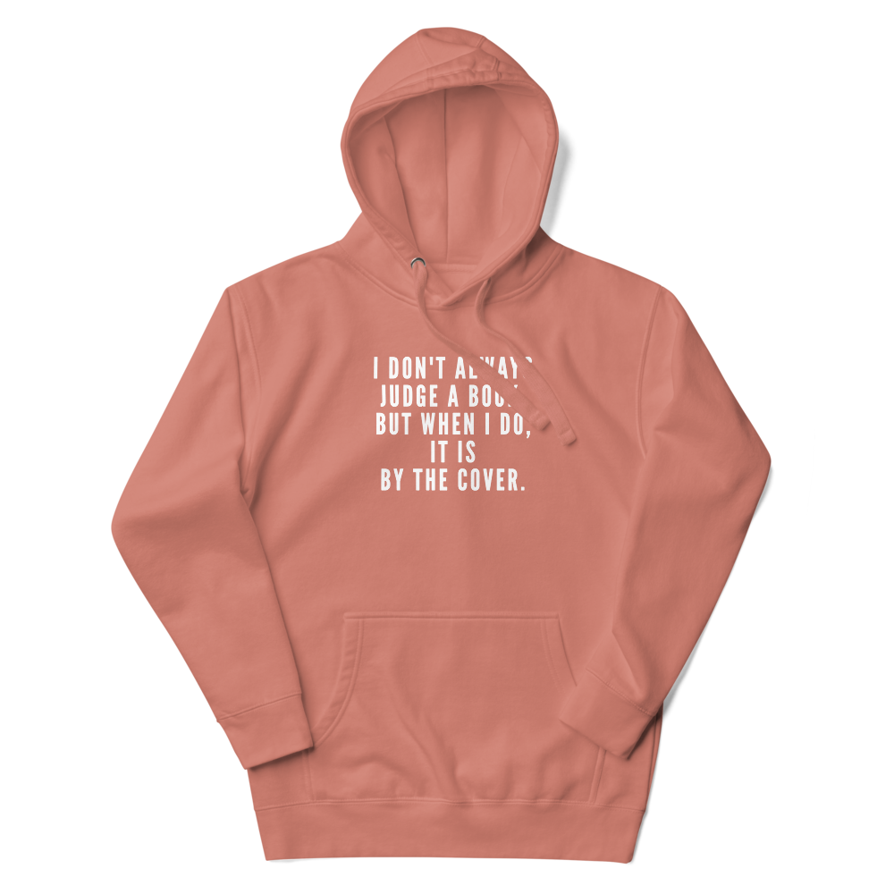 "I Don't always Judge a Book, but when I do, it's by the cover." printed on a dusty rose unisex hoodie laying on a flat surface with the hood up