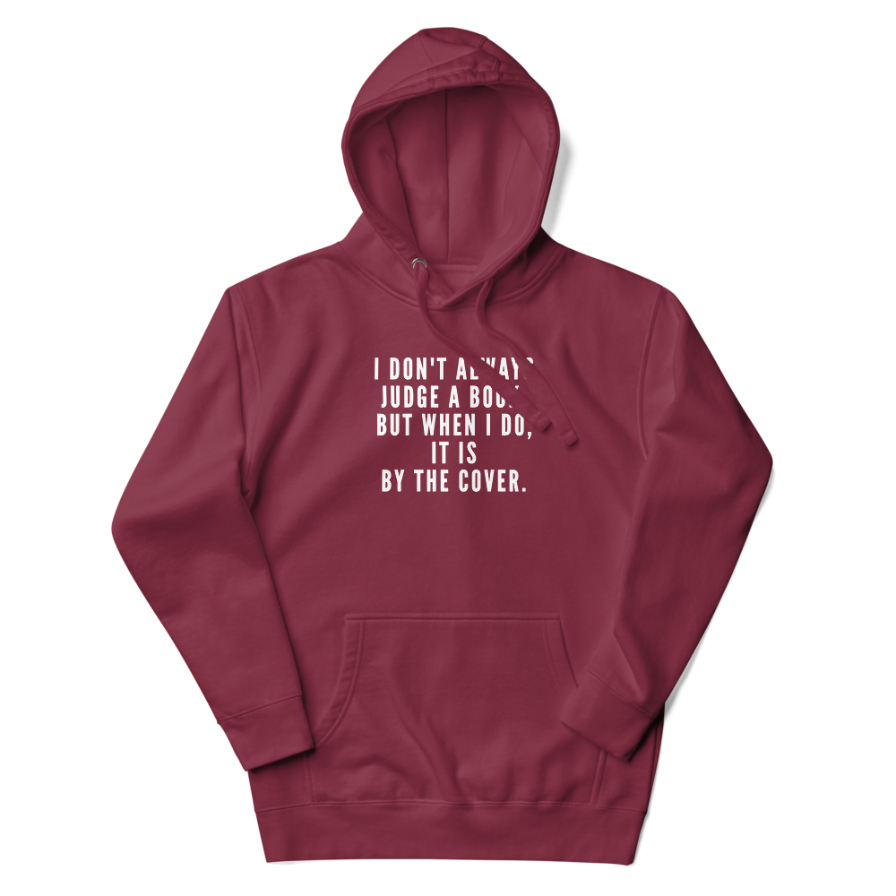 "I Don't always Judge a Book, but when I do, it's by the cover." printed on a maroon unisex hoodie laying on a flat surface with the hood up