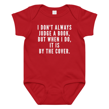 "I Don't always Judge a Book, but when I do, it's by the cover." printed on a red baby jersey bodysuit laying on a flat surface amongst other clothes