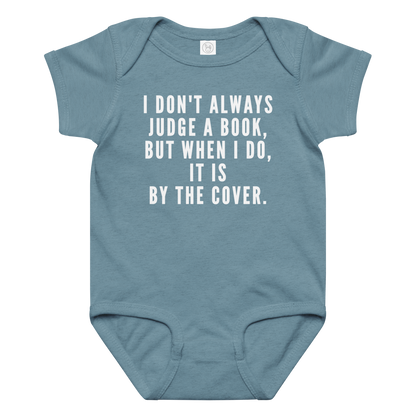 "I Don't always Judge a Book, but when I do, it's by the cover." printed on a vintage indigo baby jersey bodysuit laying on a flat surface amongst other clothes