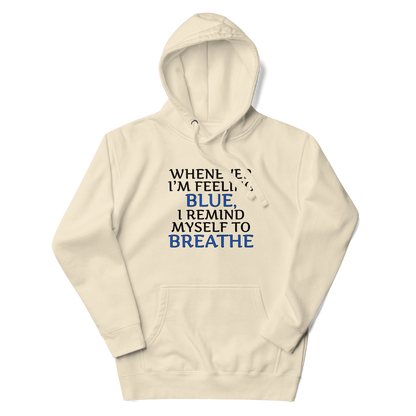 "Whenever I'm feeling blue, I remind myself to breathe" printed on a bone unisex hoodie laying on a flat surface with the hood up