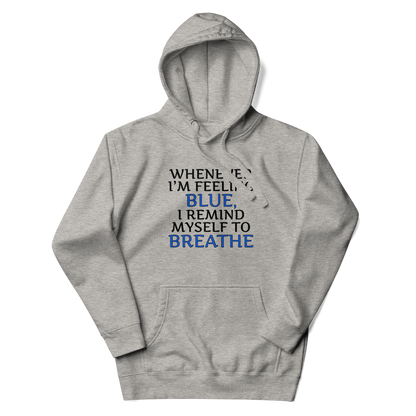 "Whenever I'm feeling blue, I remind myself to breathe" printed on a carbon grey unisex hoodie laying on a flat surface with the hood up