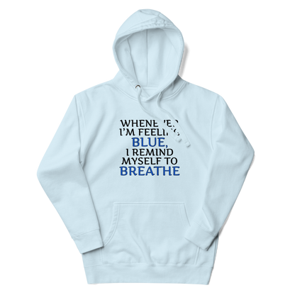"Whenever I'm feeling blue, I remind myself to breathe" printed on a sky blue unisex hoodie laying on a flat surface with the hood up