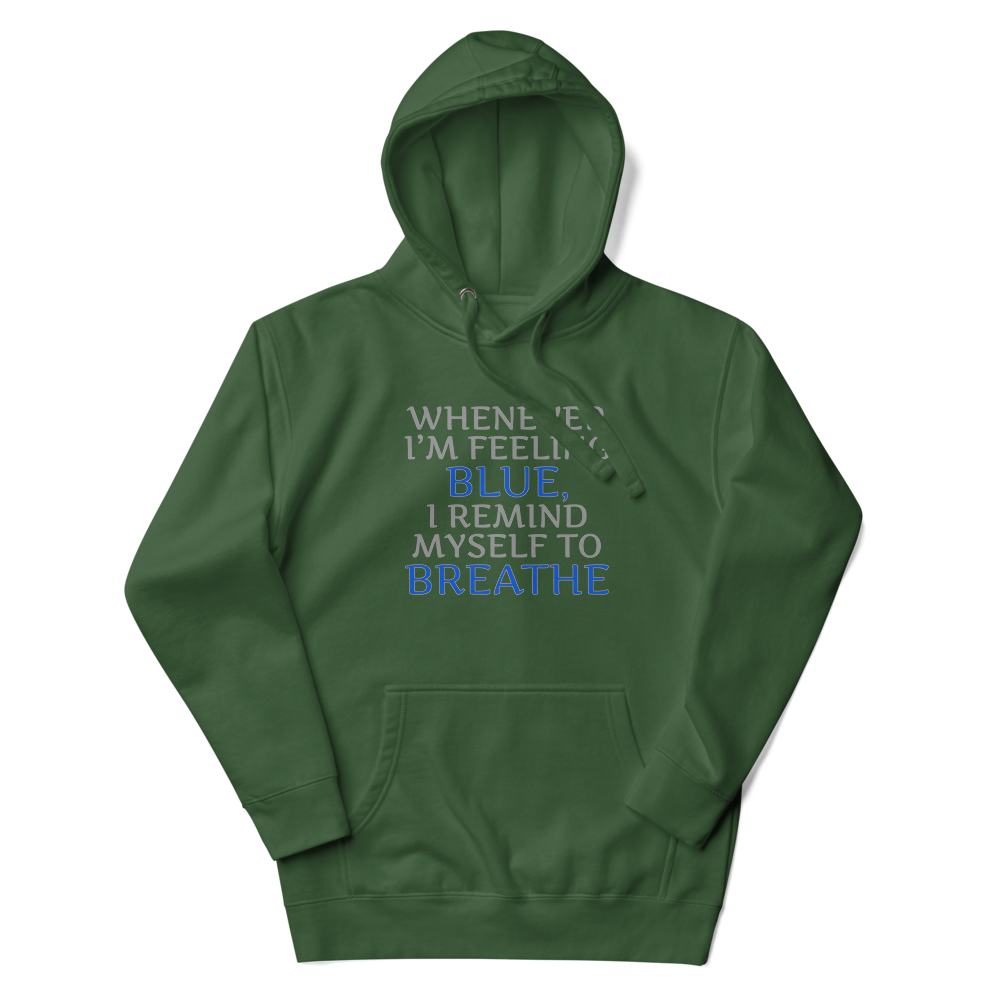 "Whenever I'm feeling blue, I remind myself to breathe" printed on a forest green unisex hoodie laying on a flat surface with the hood up