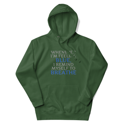 "Whenever I'm feeling blue, I remind myself to breathe" printed on a forest green unisex hoodie laying on a flat surface with the hood up