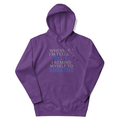 "Whenever I'm feeling blue, I remind myself to breathe" printed on a purple unisex hoodie laying on a flat surface with the hood up