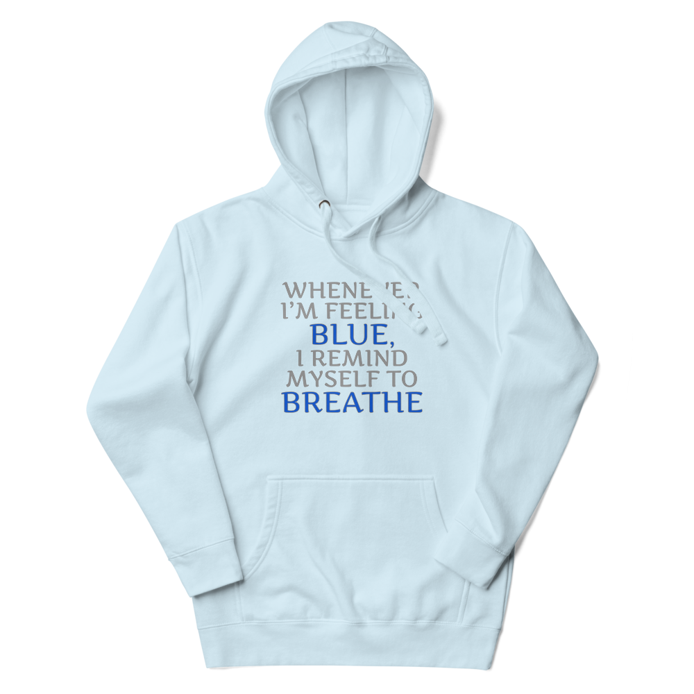 "Whenever I'm feeling blue, I remind myself to breathe" printed on a sky blue unisex hoodie laying on a flat surface with the hood up