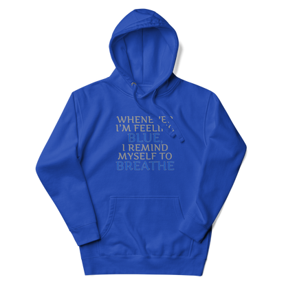 "Whenever I'm feeling blue, I remind myself to breathe" printed on a team royal unisex hoodie laying on a flat surface with the hood up