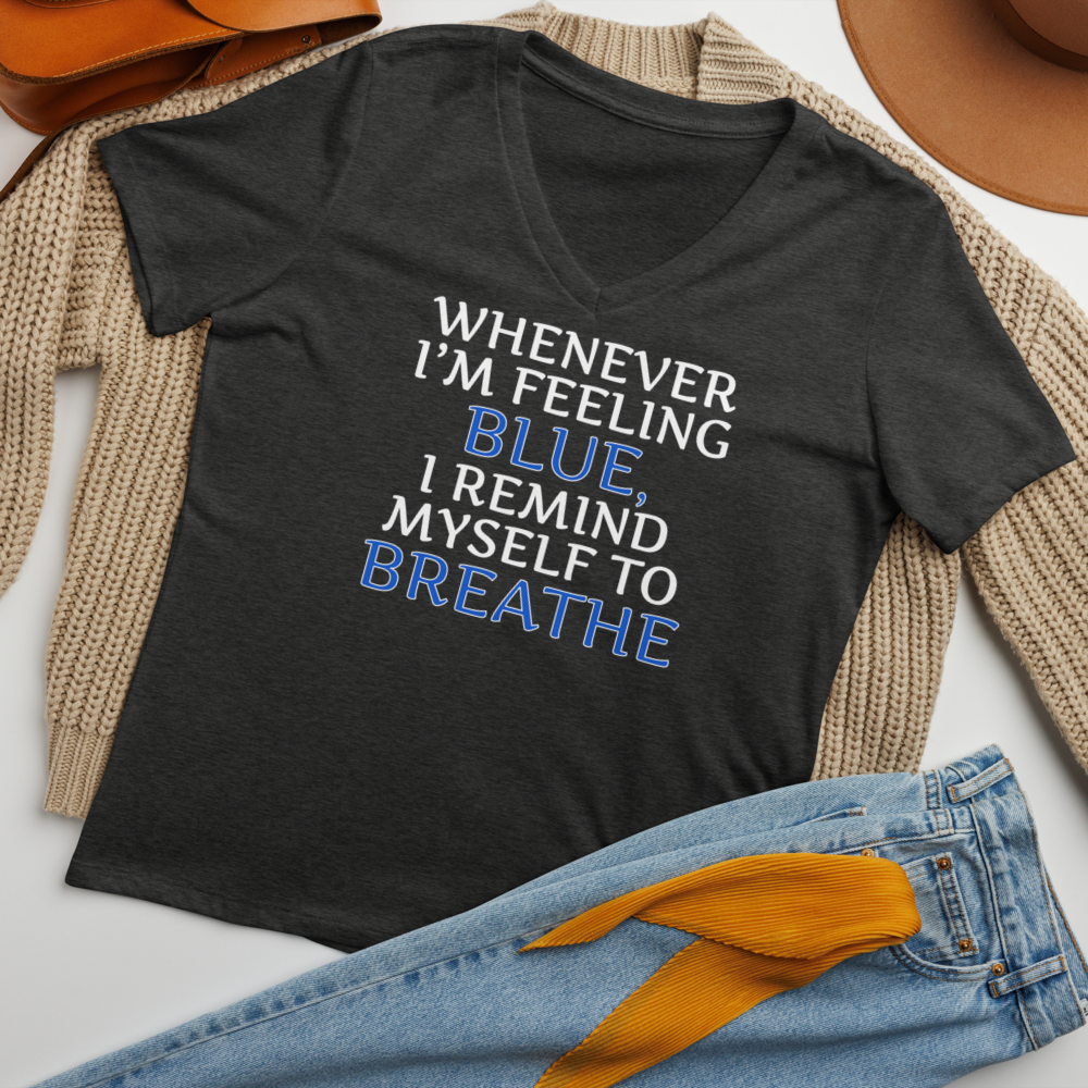 "Whenever I'm feeling blue, I remind myself to breathe" printed on a dark grey heather women's relaxed v-neck t-shirt laying on a flat surface amongst other clothes