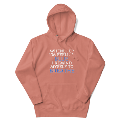"Whenever I'm feeling blue, I remind myself to breathe" printed on a dusty rose unisex hoodie laying on a flat surface with the hood up