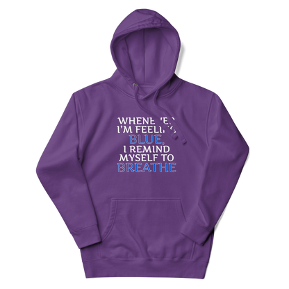 "Whenever I'm feeling blue, I remind myself to breathe" printed on a purple unisex hoodie laying on a flat surface with the hood up