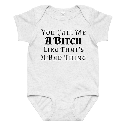 "You Call Me A Bitch Like That's A Bad Thing" printed on a ash baby jersey bodysuit laying on a flat surface amongst other clothes