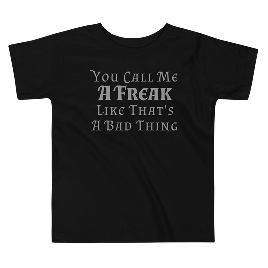 "You Call Me A Freak Like That's A Bad Thing" printed on a black toddler short sleeve tee laying on a flat surface