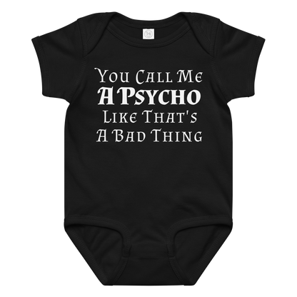 "You Call Me A Psycho Like That's A Bad Thing" printed on a black baby jersey bodysuit laying on a flat surface amongst other clothes