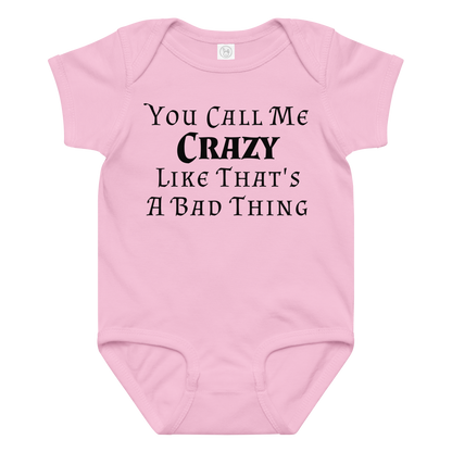 "You Call Me Crazy Like That's A Bad Thing" printed on a pink baby jersey bodysuit laying on a flat surface amongst other clothes