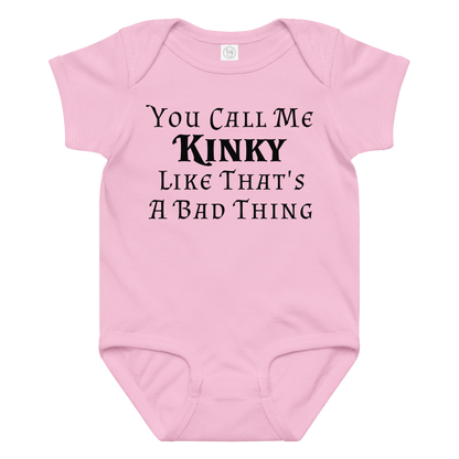 "You Call Me Kinky Like That's A Bad Thing" printed on a pink baby jersey bodysuit laying on a flat surface amongst other clothes